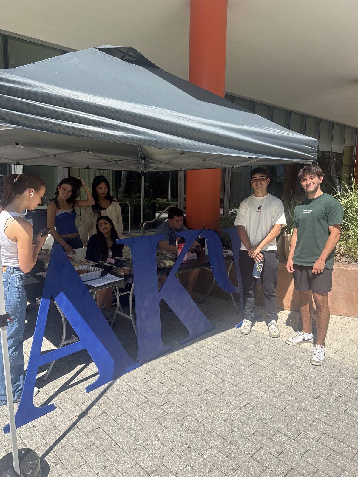 Brothers by the AKPsi letters at the bake sale tent